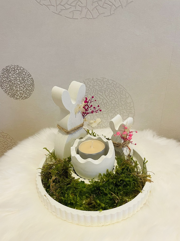 Dekoriertes Osternest mit zwei Hasen und einem Ei mit Kerze auf Grundplatte